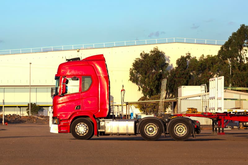 Röd dragbil utan släp parkerad på en industriplan